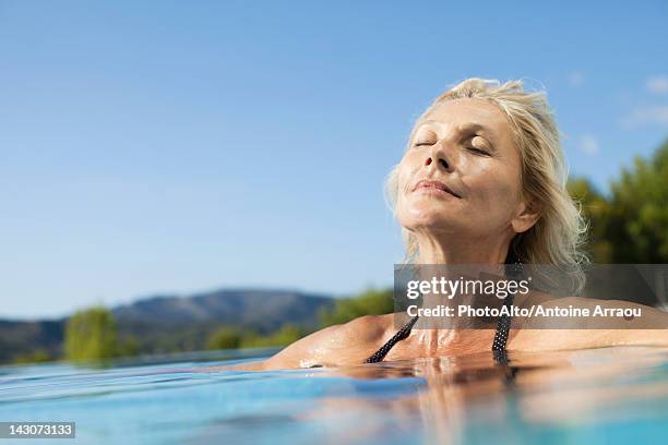 mature woman relaxing in pool with eyes closed - women sunbathing pool stock pictures, royalty-free photos & images