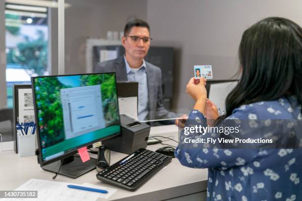 cajero bancario comprobando la licencia de conducir del cliente - carnet fotografías e imágenes de stock