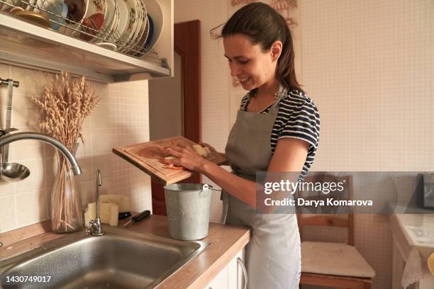 a woman stands in the kitchen and cooks a dinner of vegetables. a woman uses a compost bucket. vegetarian food. organic processing of vegetable household waste. - peeling food stock pictures, royalty-free photos & images