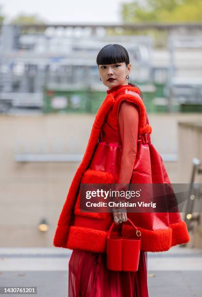 Kozue Akimoto wears red shearling sleeveless jacket, bucket bag, see trough skirt outside Sacai during Paris Fashion Week - Womenswear Spring/Summer...