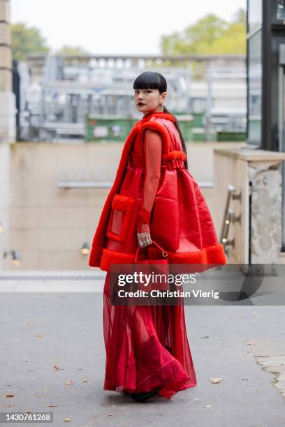 Kozue Akimoto wears red shearling sleeveless jacket, bucket bag, see trough skirt outside Sacai during Paris Fashion Week - Womenswear Spring/Summer...