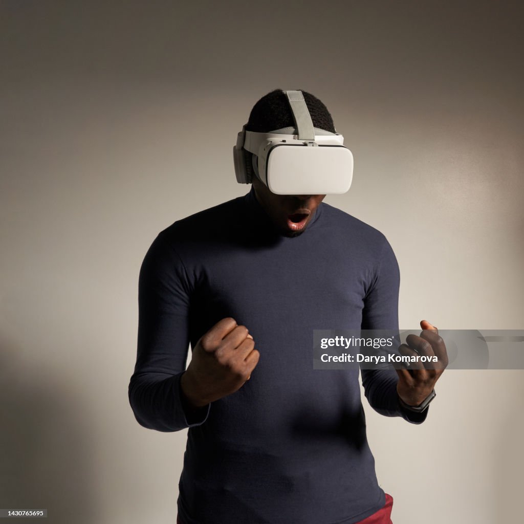 A young African-American man in VR glasses with strong emotions. The concept of the future, computer games, augmented reality, virtual reality, modern technologies, technological progress, escapism.