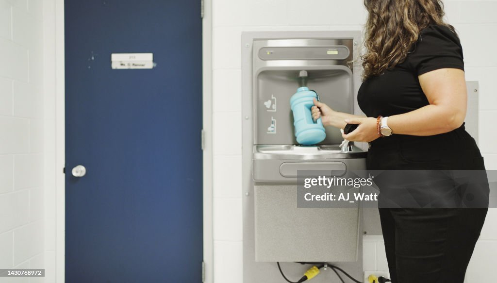 School teacher refilling her water bottle at a hallway fountain