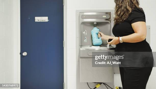 school teacher refilling her water bottle at a hallway fountain - drinking fountain stock pictures, royalty-free photos & images