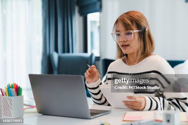 young girl wear headphones using laptop learn online and writing notebook in living room at home. - vertaling stockfoto's en -beelden