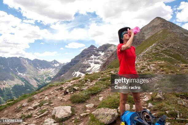 mature woman backpacker resting and drinking water on top of buckskin pass. four pass backpacking trip around the maroon bells. aspen, colorado. - maroon bells summer stock pictures, royalty-free photos & images