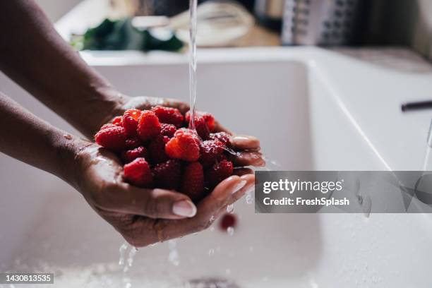 eine seitenansicht einer unkenntlichen frau, die himbeeren wäscht - raspberry stock-fotos und bilder
