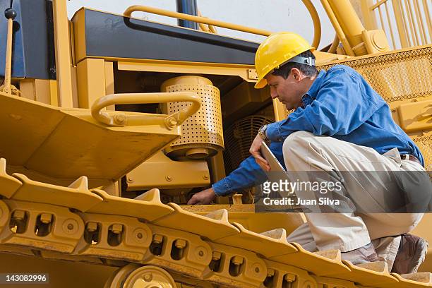 man on bulldozer with tablet looking at engine - baumaschine stock-fotos und bilder