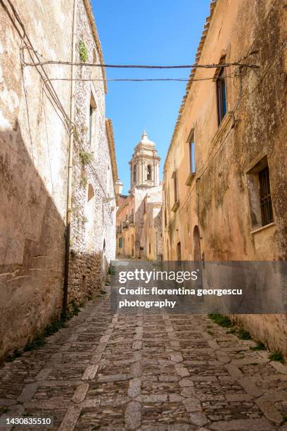 atmospheric cobbled street and the bell tower of the chiesa di san giuliano in the medieval town of erice, sicily, italy - erice imagens e fotografias de stock