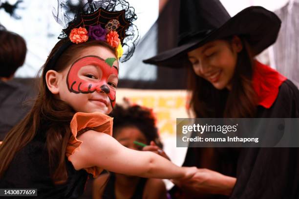 beautiful mother dress witch dress make halloween painting on face of her daughter, halloween celebration concept - face painting imagens e fotografias de stock