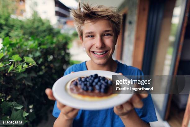 teenage boy holding a plate with pancake topped with chocolate and blueberries - blueberry pancakes stock pictures, royalty-free photos & images