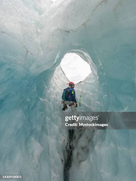 homme grimpant sur la glace à l’intérieur d’une crevasse glaciaire en islande - crevasse photos et images de collection