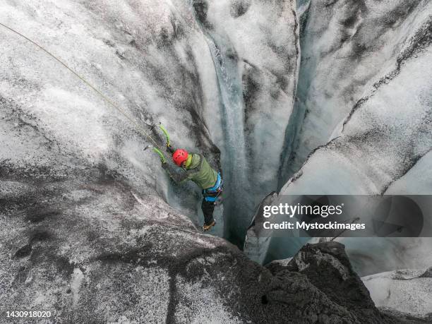 homme grimpant sur la glace à l’intérieur d’une crevasse glaciaire en islande - crevasse photos et images de collection