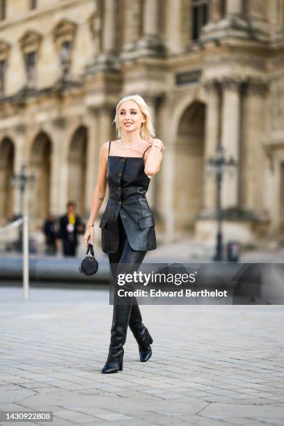 Emma Chamberlain wears gold earrings, a black shiny leather square-neck / buttoned long tank-top, black shiny leather legging pants, black shiny...