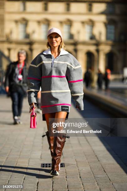 Veronica Ferraro wears a pale pink cap, a gray with white latte and neon pink striped embroidered pattern oversized sweater short dress from Louis...