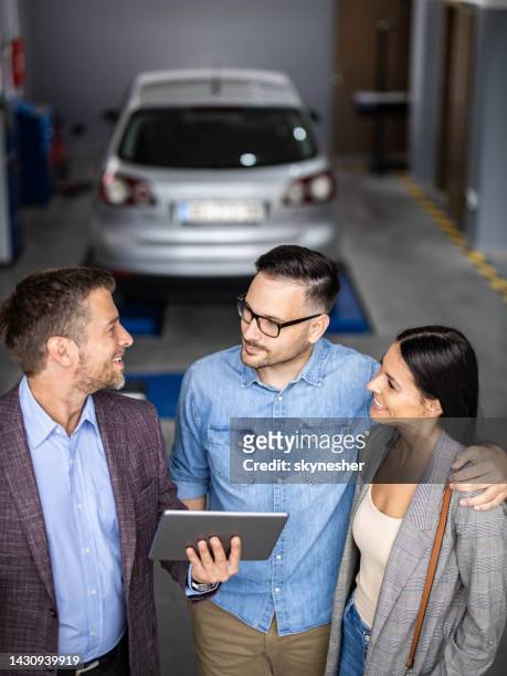 happy salesman talking to a couple in auto repair shop. - touchpad stockfoto's en -beelden