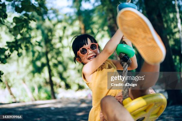 joyful little asian girl with sunglasses having fun playing on a zipline in an adventure park outdoors on a sunny day. adventurous and active lifestyle of children. outdoor fun - natural land state stock pictures, royalty-free photos & images