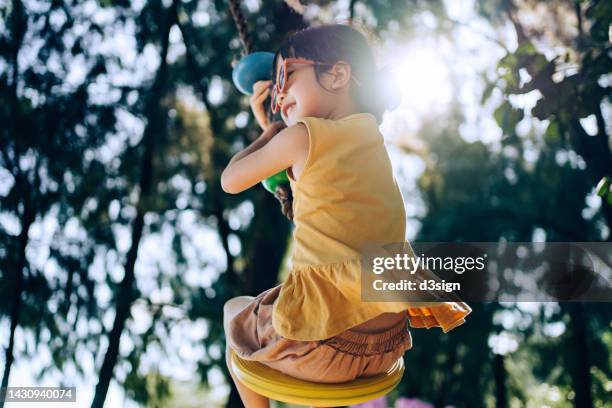 joyful little asian girl with sunglasses having fun playing on a zipline in an adventure park outdoors on a sunny day. adventurous and active lifestyle of children. outdoor fun - asian games day 1 stock-fotos und bilder