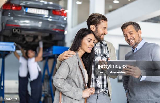 happy manager and young couple using touchpad in auto repair shop. - touchpad stockfoto's en -beelden