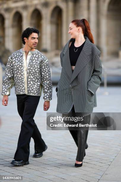 Joe Jonas wears a white with silver embroidered pearls leopard print pattern jacket, black flared pants, black shiny leather shoes , ; Sophie Turner...