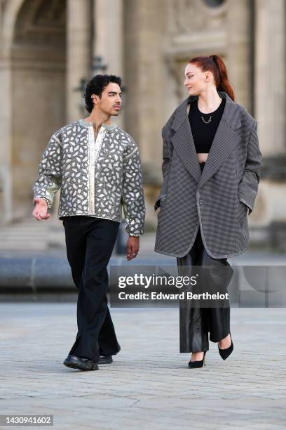 Joe Jonas wears a white with silver embroidered pearls leopard print pattern jacket, black flared pants, black shiny leather shoes , ; Sophie Turner...