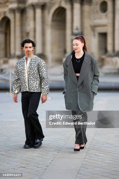 Joe Jonas wears a white with silver embroidered pearls leopard print pattern jacket, black flared pants, black shiny leather shoes , ; Sophie Turner...