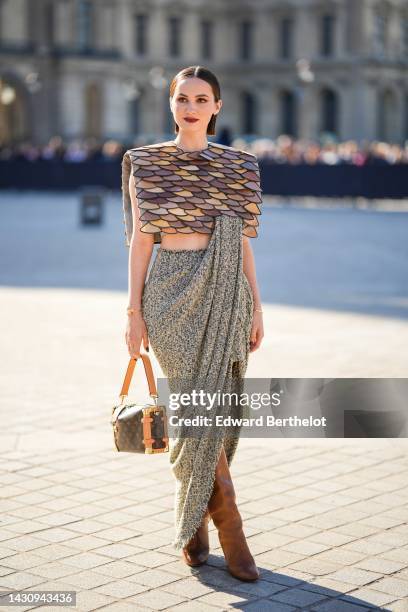 Maude Apatow wears gold earrings, a brown and beige shiny leather embroidered yoke shoulder-pads / sleeveless cropped top from Louis Vuitton, a khaki...