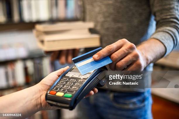 unkenntliche person, die mit einer kreditkarte für bücher in der modernen buchhandlung bezahlt - buchhändler stock-fotos und bilder
