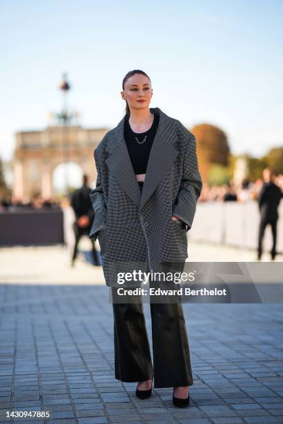 Sophie Turner wears a black cropped tank-top with a silver chain necklace, a black and white small checkered print pattern oversized jacket, black...