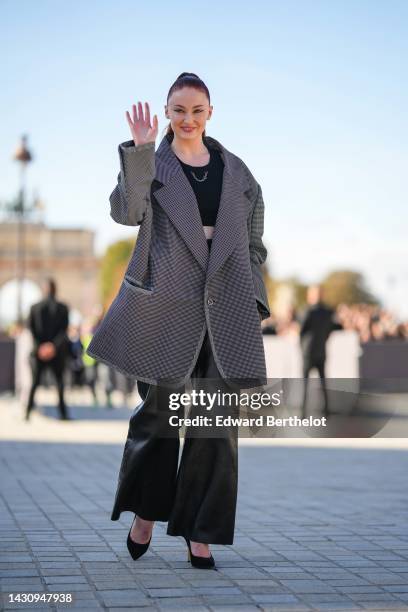 Sophie Turner wears a black cropped tank-top with a silver chain necklace, a black and white small checkered print pattern oversized jacket, black...