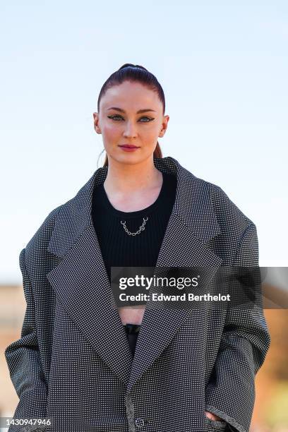 Sophie Turner wears a black cropped tank-top with a silver chain necklace, a black and white small checkered print pattern oversized jacket, black...