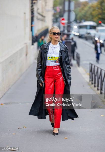 Caroline Caro Daur wears black leather jacket, red varnished pants, white shirt with words print outside Sacai during Paris Fashion Week - Womenswear...