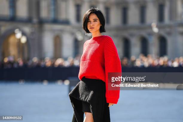 Kelsey Asbille wears a red ribbed wool oversized pullover, a black felt asymmetric long train skirt from Louis Vuitton, outside Louis Vuitton, during...