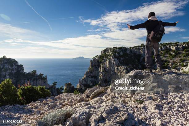 rear view of a man standing on rocks with outstretched arms, les calanques, cassis, bouches-du-rhone, provence-alpes-cote d'azur, france - cassis stock-fotos und bilder