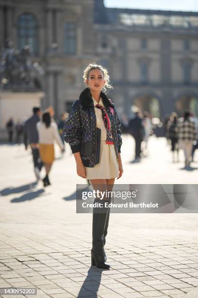 Emili Sindlev wears gold earrings, a black with multicolored print pattern oversized bomber coat with black sheep collar from Louis Vuitton, a black...