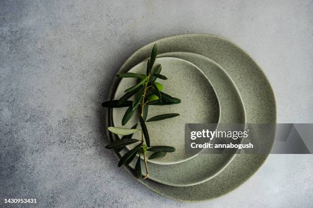 overhead view of an olive branch on a stack of rustic ceramic plates - olive branch stock pictures, royalty-free photos & images