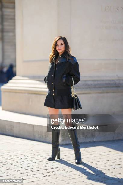 Ana de Armas wears a black shiny leather shoulder and black embossed LV monogram print pattern fabric buttoned bomber coat, a black tank-top, black...