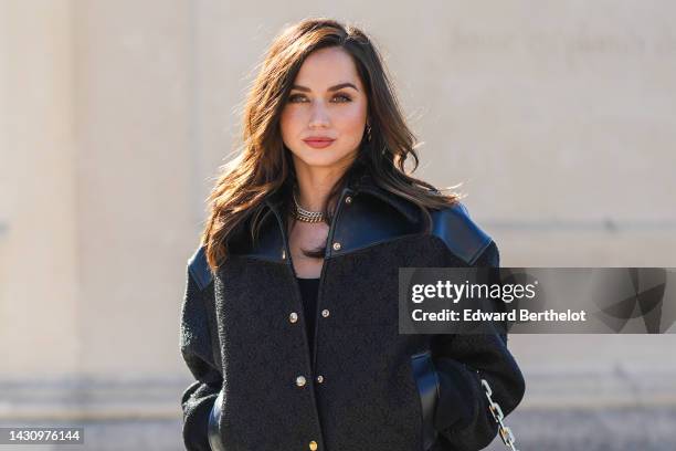 Ana de Armas wears a black shiny leather shoulder and black embossed LV monogram print pattern fabric buttoned bomber coat, a black tank-top, black...