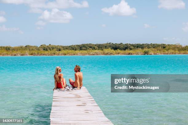 couple relaxing on wooden pier above beautiful blue lagoon - escapismo imagens e fotografias de stock