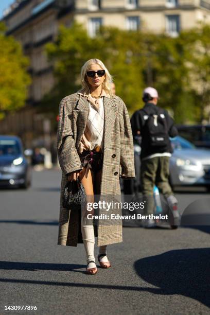 Caroline Daur wears black sunglasses from Miu Miu, a gold large chain necklace, a beige and white checkered print pattern wool polo shirt, brown and...