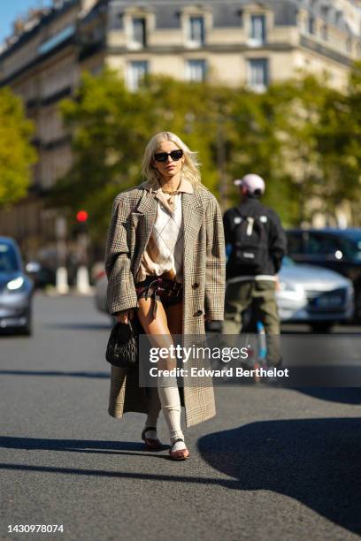 Caroline Daur wears black sunglasses from Miu Miu, a gold large chain necklace, a beige and white checkered print pattern wool polo shirt, brown and...