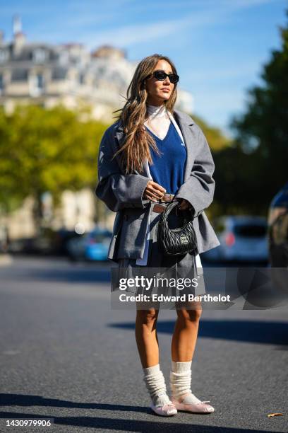 Tamara Kalinic wears black sunglasses, a white tulle turtleneck top, a navy blue wool pullover from Miu Miu, a pale gray oversized jacket from Miu...