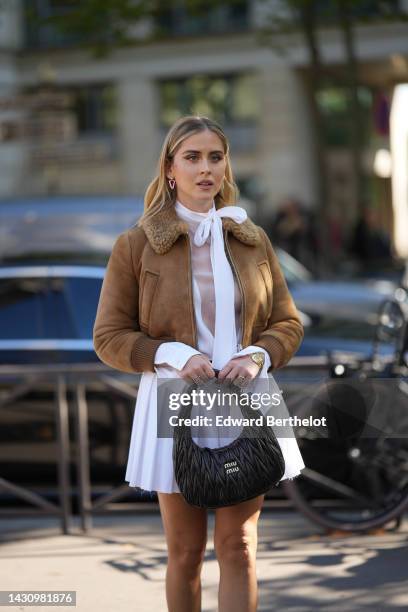 Valentina Ferragni wears blue and pink earrings, a white tulle knot high neck transparent t-shirt, a brown shiny leather bomber coat with sheep...