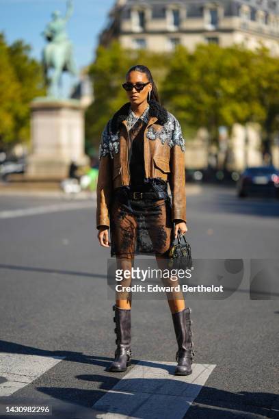 Cindy Bruna wears black sunglasses, diamonds long earrings, a black lace print pattern with diamonds embroidered collar shirt short dress , a brown...