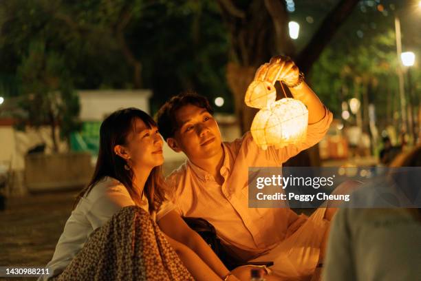 young happy asian couple watching the light and having fun with lanterns to celebrate mid-autumn festival - mid autumn festival stock pictures, royalty-free photos & images