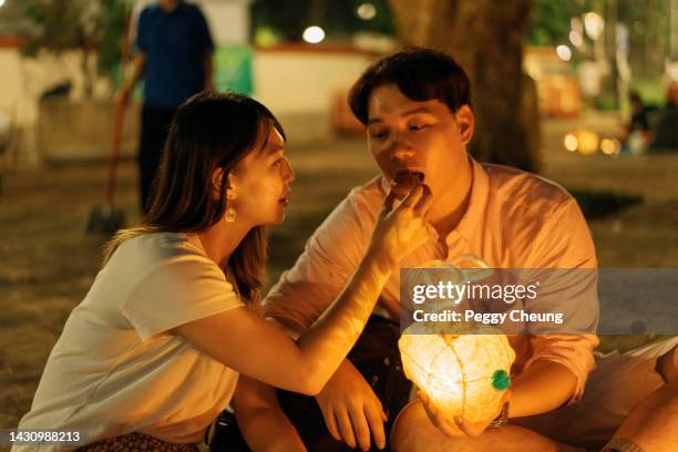 young happy asian couple eating mooncake and having fun with traditional lanterns to celebrate mid-autumn festival - mid autumn festival stock pictures, royalty-free photos & images