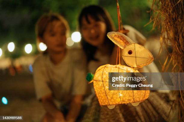 una tradizionale lanterna cinese a forma di coniglio di carta appesa a un albero mentre due giovani sorelle asiatiche felici o amiche celebrano il mid-autumn festival - festival delle lanterne cinesi foto e immagini stock