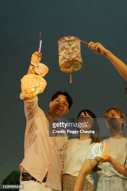 young asian friends holding traditional paper lantern while celebrating chinese mid-autumn festival outdoors at night together - 元宵節 個照片及圖片檔