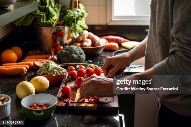 human hands slicing tomatoes over a wooden table for a vegan meal - préparation des aliments photos et images de collection