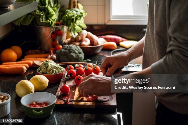 human hands slicing tomatoes over a wooden table for a vegan meal - alimentazione sana foto e immagini stock